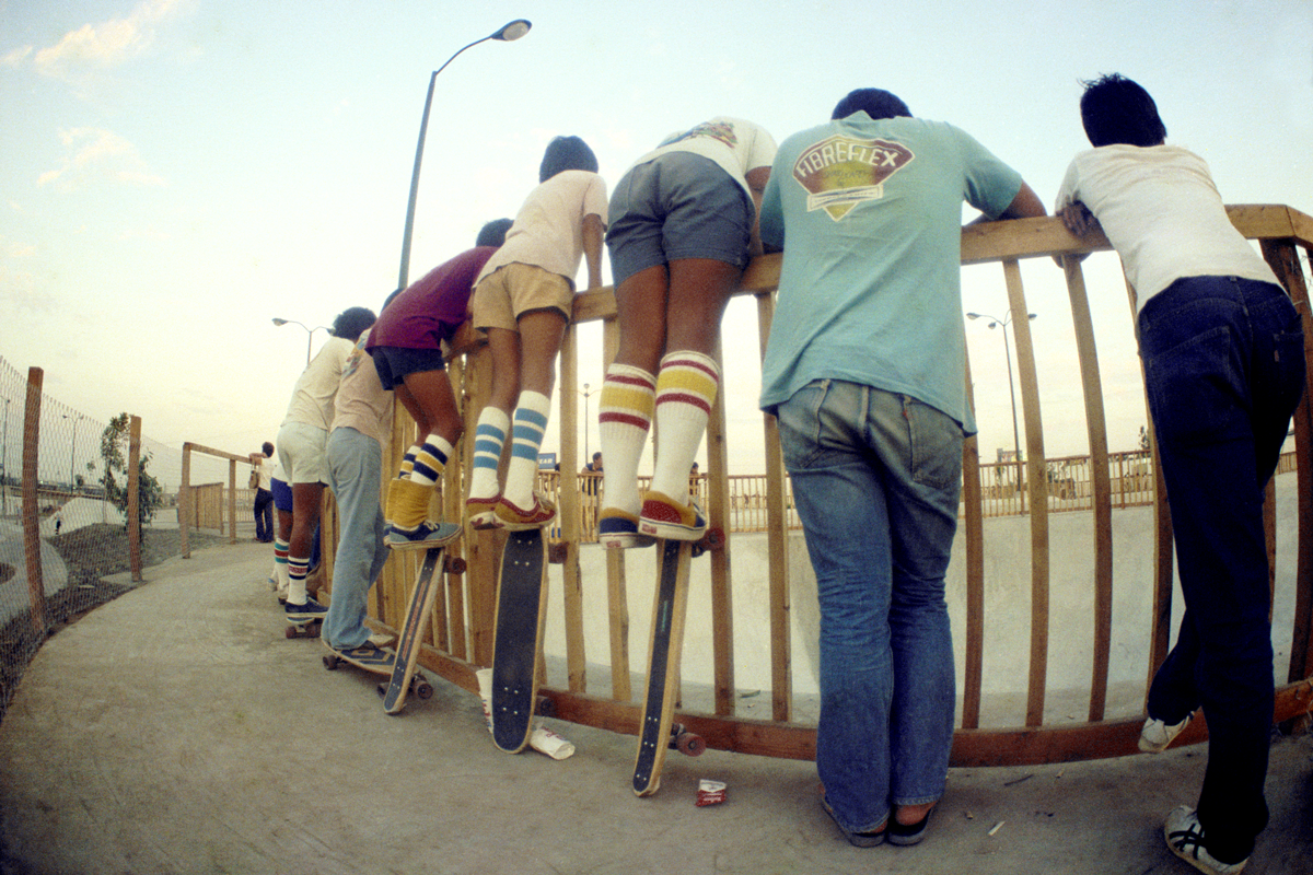 Hugh Holland photograph of kids leaning against a fence watching a skateboarder