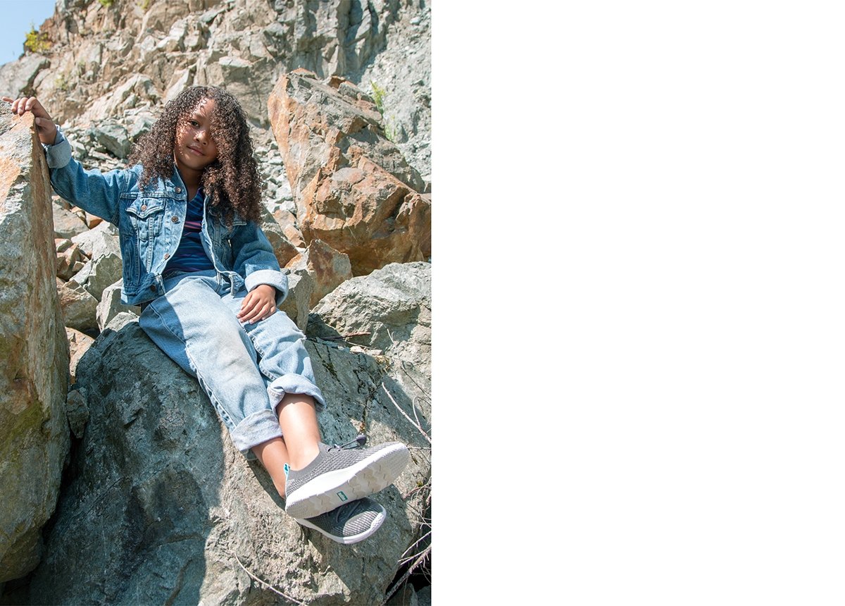 Girl is sitting on a rock and wearing slip on knit sneakers.