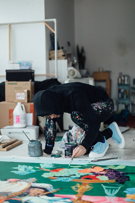 Artist Andy Dixon paints on floor wearing black hoody and Jefferson Sneakers by Native Shoes.