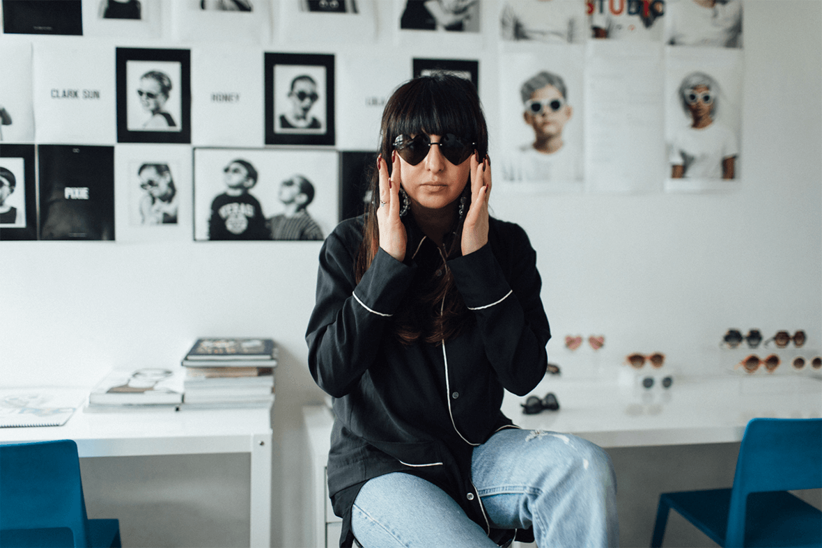 Shiva Shabani wears sunglasses and the Native Shoes Jefferson 2.0 low on a stool in her studio for Sons and Daughters eyewear.