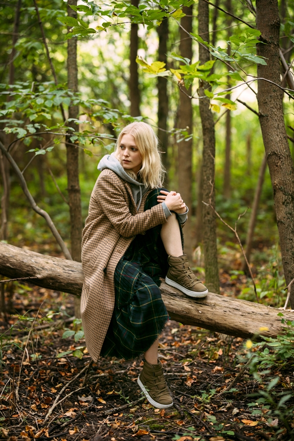 Woman wearing the Chamonix winter boots with a winter outfit in the woods sitting on a log