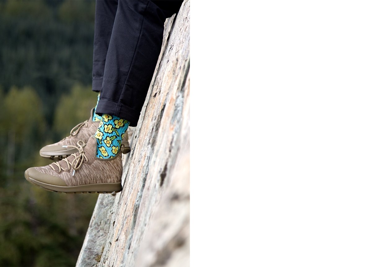 Feet wearing cool shoes and colorful socks on rocky cliff.