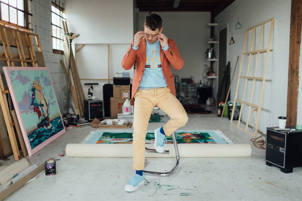Artist Andy Dixon in his studio sitting on a stool wearing Native Shoes Jefferson 2.0