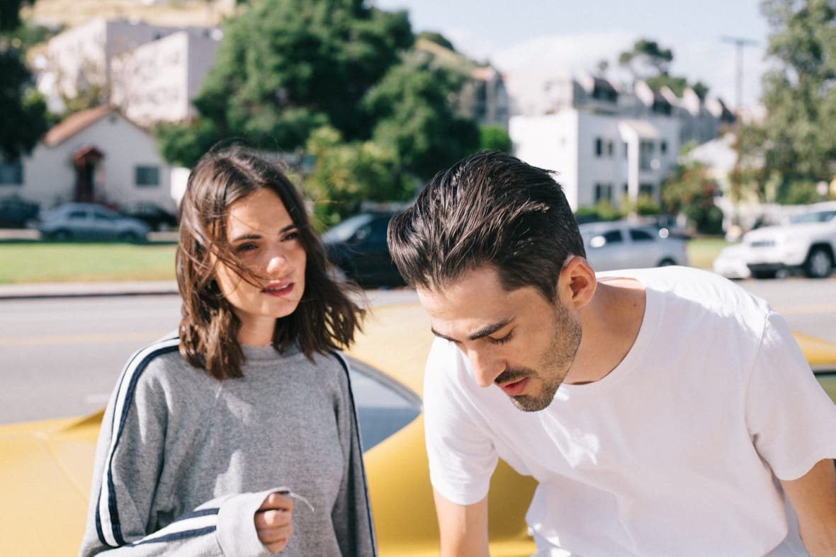 Girl with wind-blown hair speaking to guy in front of yellow sports car