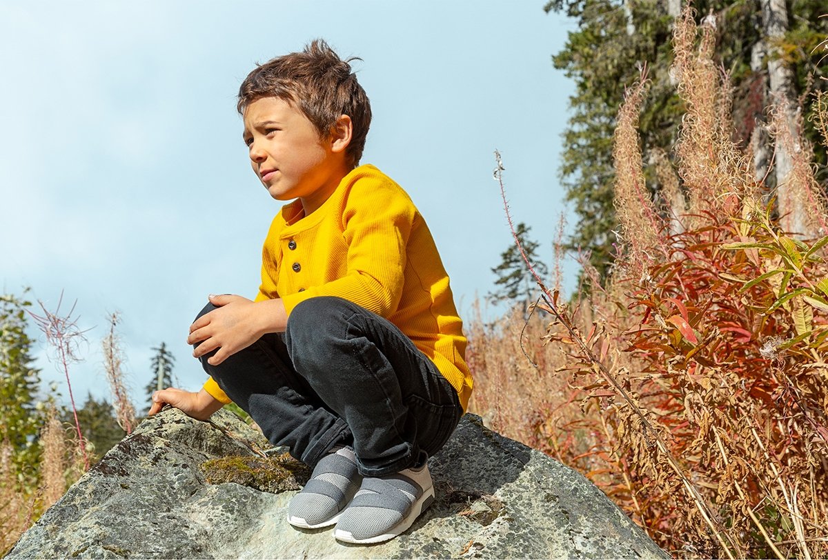 Kid wearing slip-on sneakers in forest.