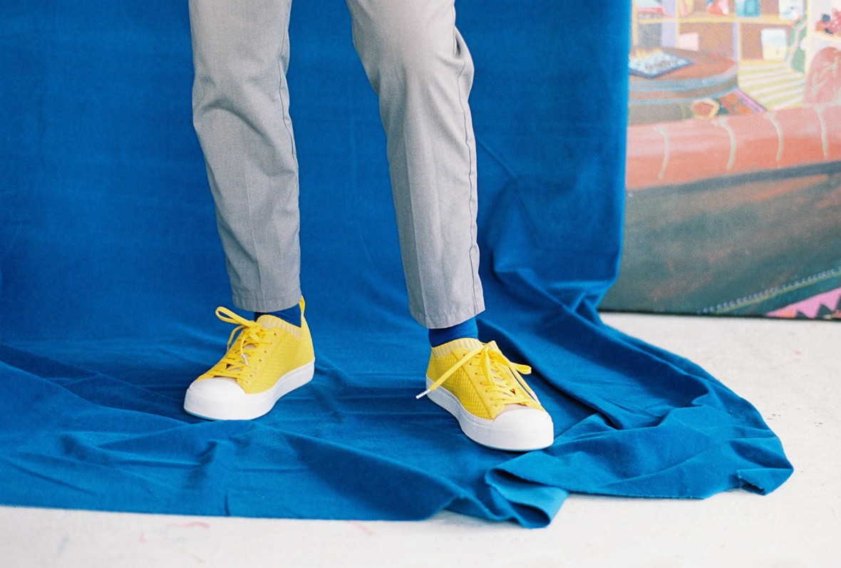 Wearing yellow Native Shoes Jefferson 2.0 on a blue backdrop