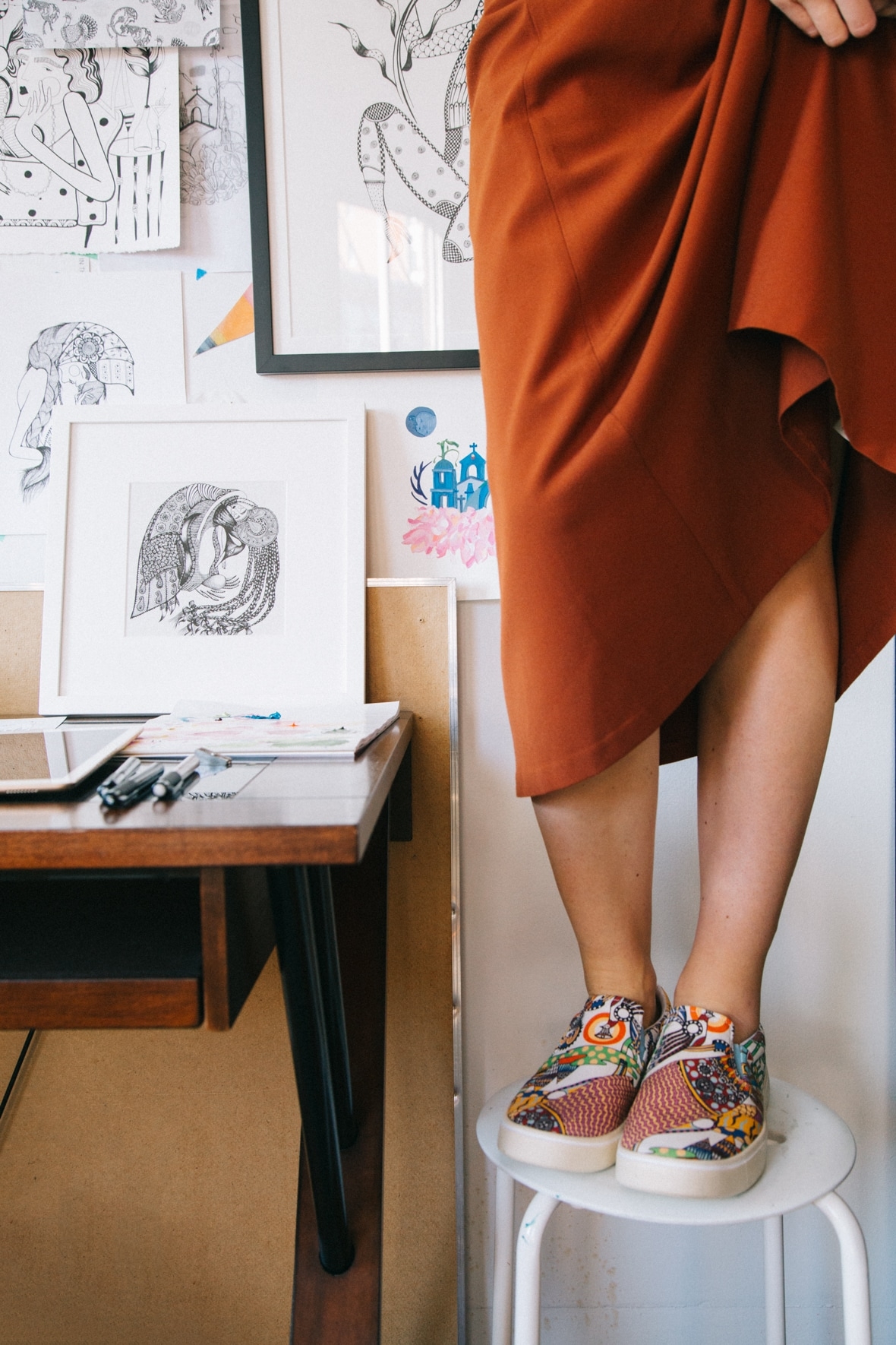 Ola Volo wearing the Native Shoes Ola Volo print collaboration shoes standing on a stool in her studio.