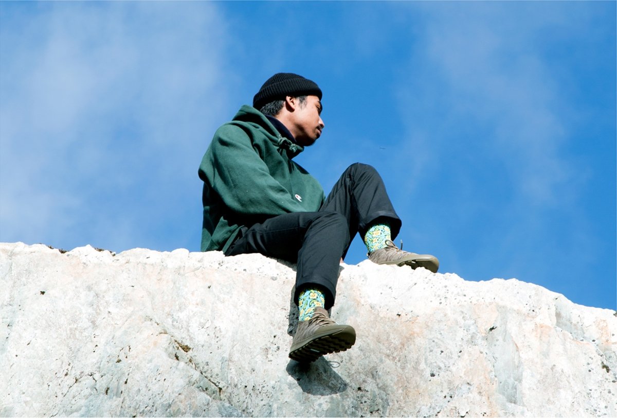 Guy wearing cool sneakers sits on rocky cliff.
