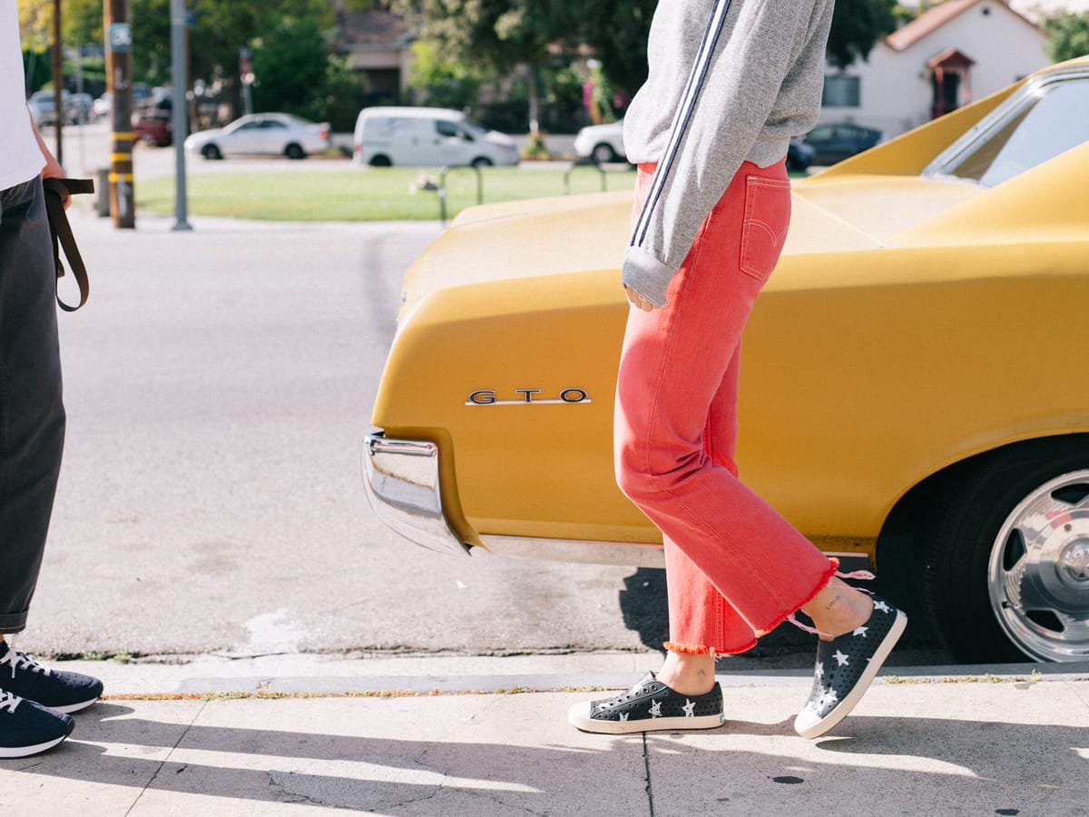 Girl in star-print sneakers wearing pink pants walks beside yellow vintage car