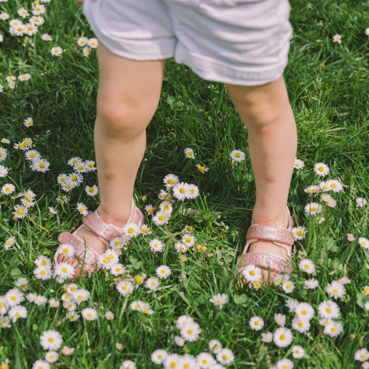 A child standing in flowers wearing the Chase kids sandal by Native Shoes