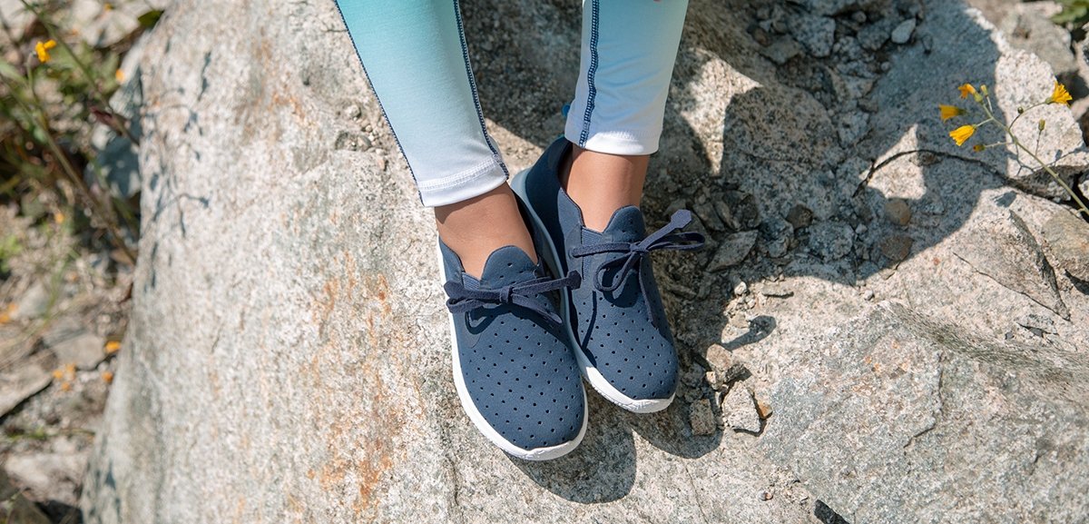 Girl is wearing slip on sneakers on rock.