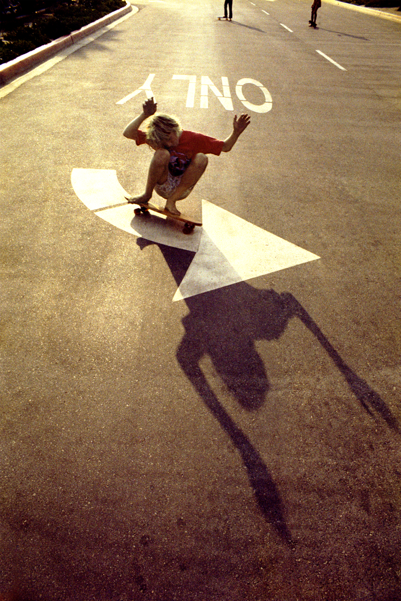 Hugh Holland photograph of kid skateboarding down road