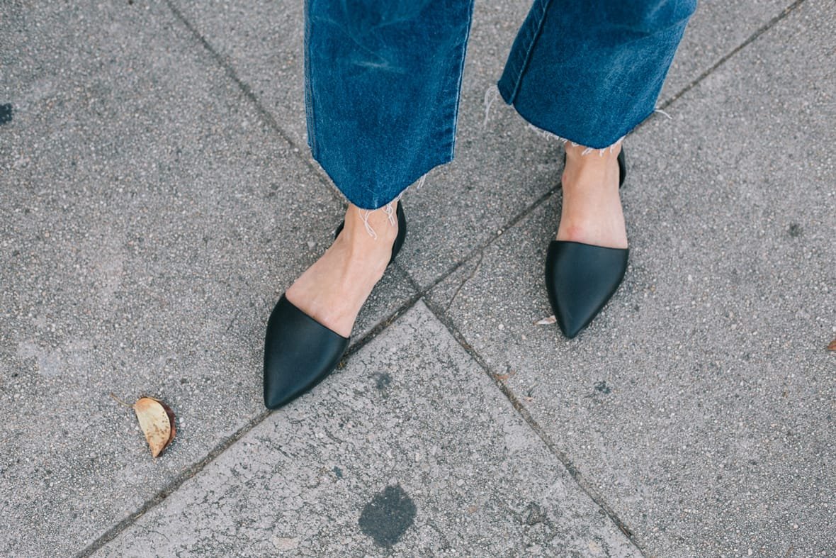 Women's feet wearing denim and black slip-on flat shoes with pointed toe
